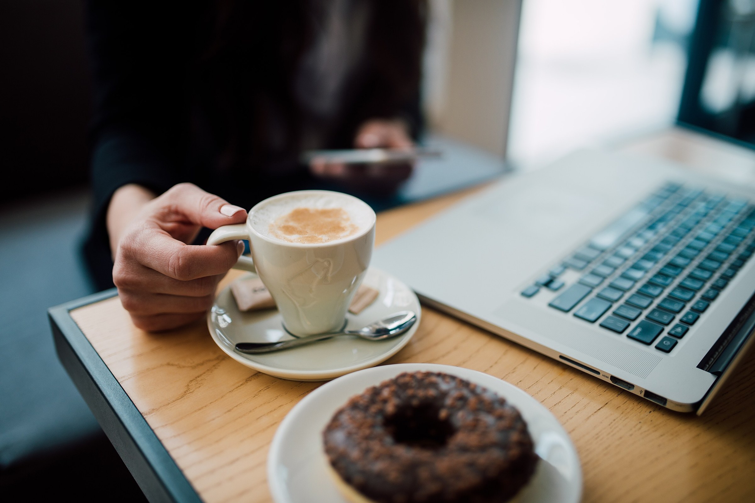 A traveler holds a smartphone over coffee next to a laptop