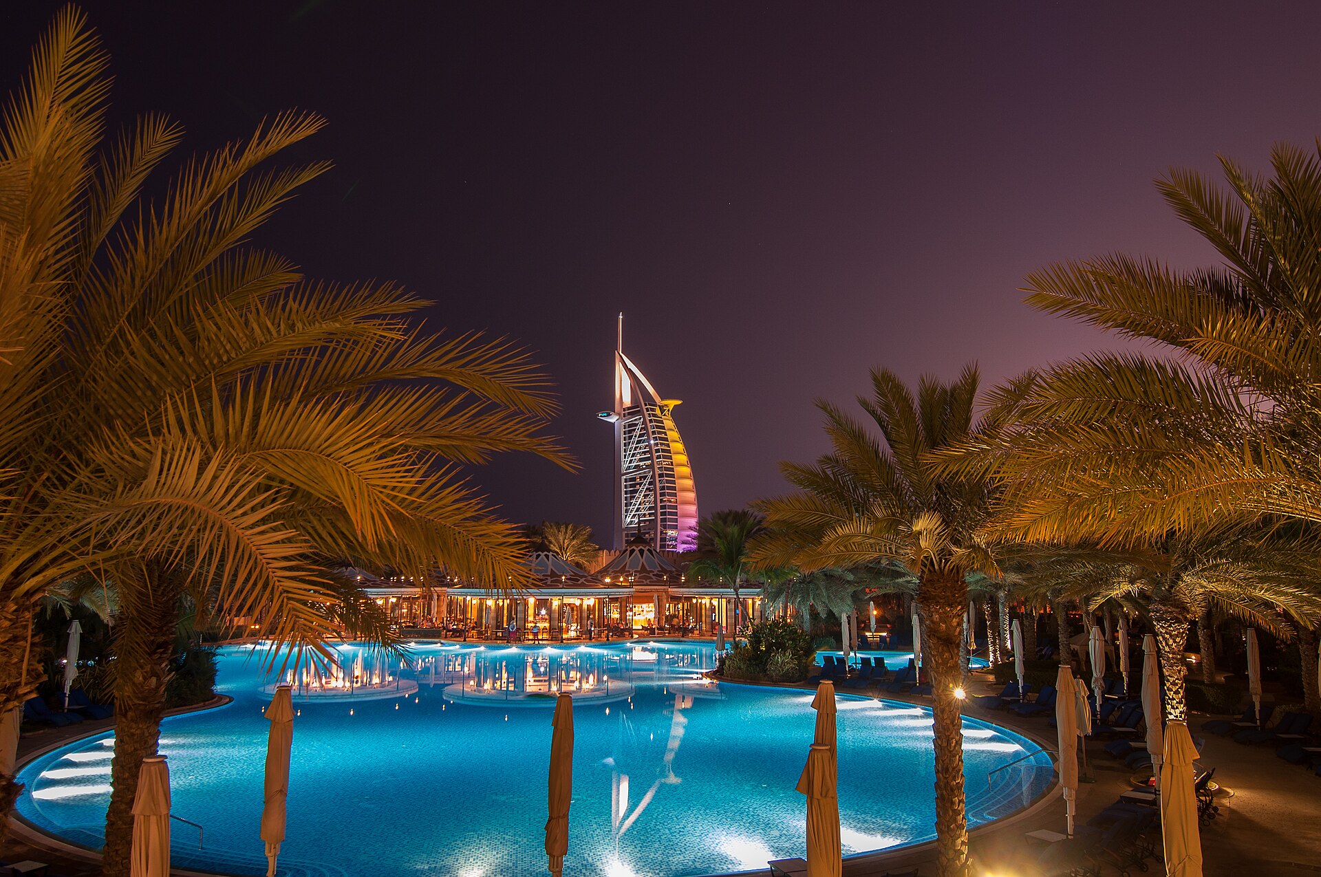 The Burj Al Arab lit up at night behind a resort pool lined with palm trees