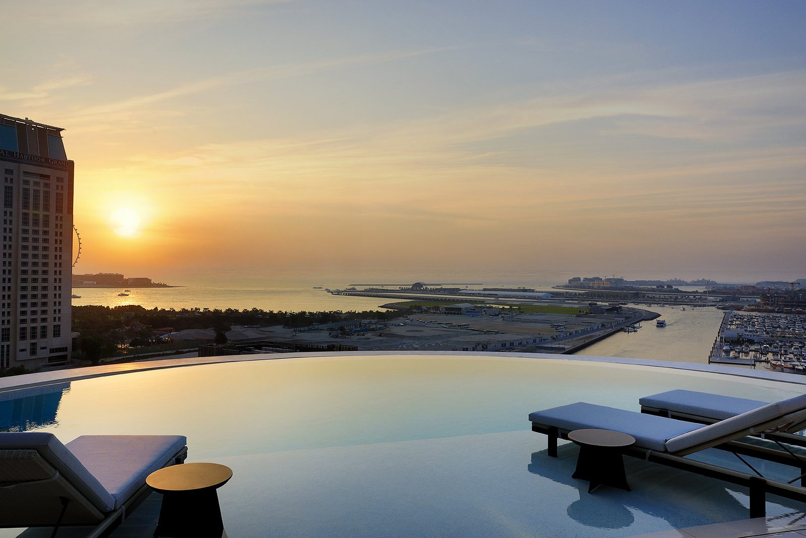 An infinity-edge outdoor pool deck at Ciel Dubai Marina at sunset, looking out over Dubai Harbour and the Gulf