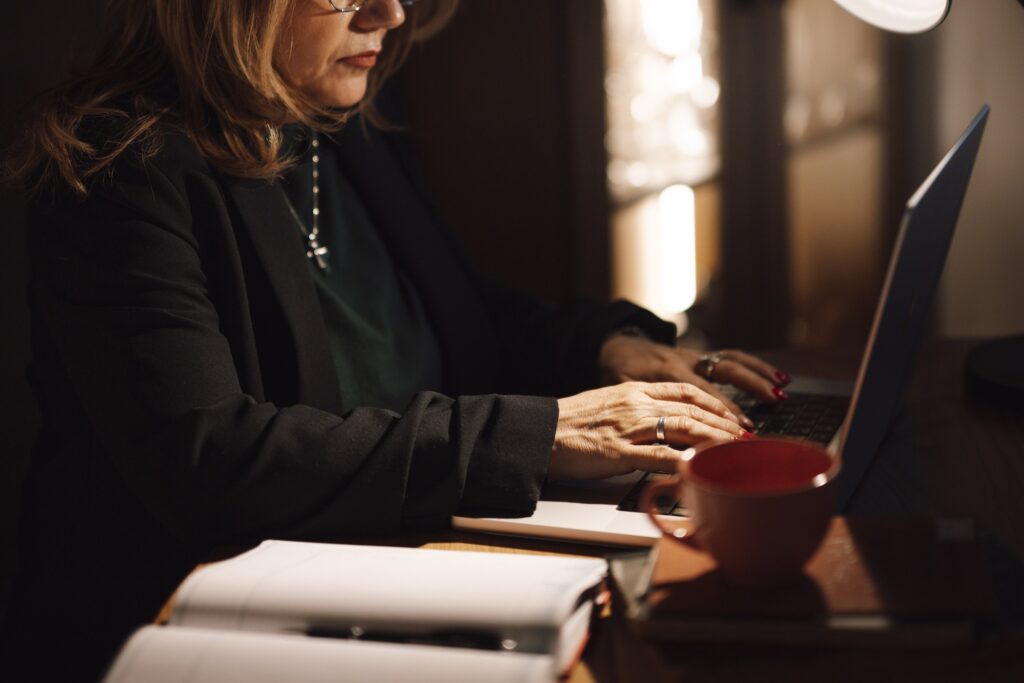 A businesswoman typing on a laptop beside a red coffee cup and an open notebook