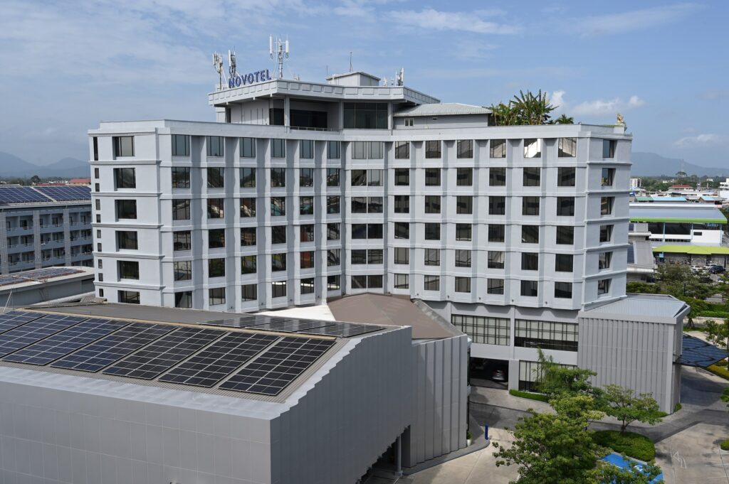 A modern mid-rise hotel complex under a blue sky with rooftop solar panels in the foreground