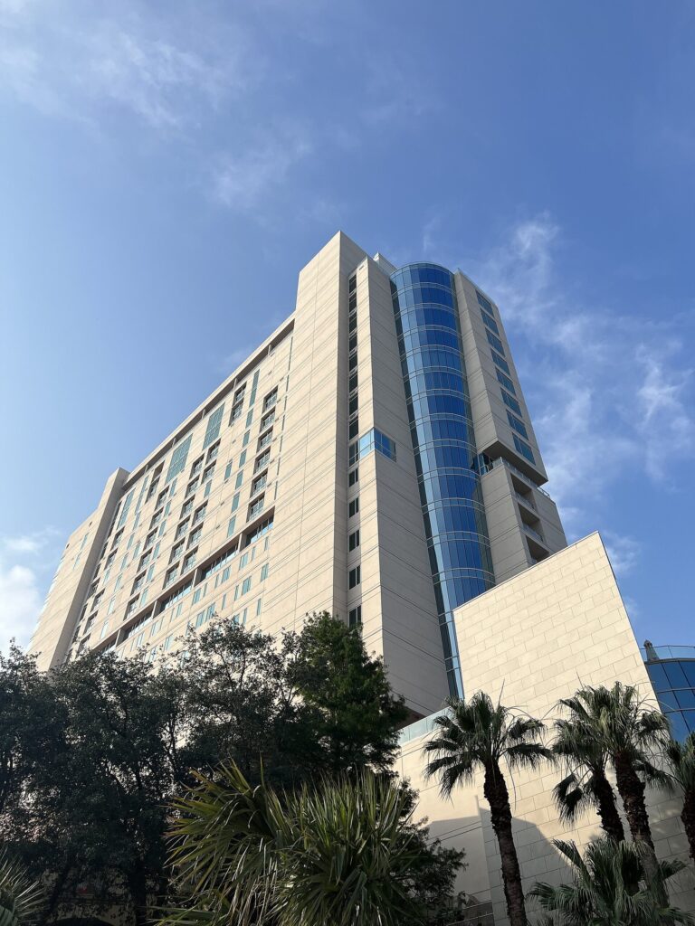 The 20-story Arts Residences tower in downtown San Antonio, home of the Thompson San Antonio hotel, against a blue sky with palm trees in front